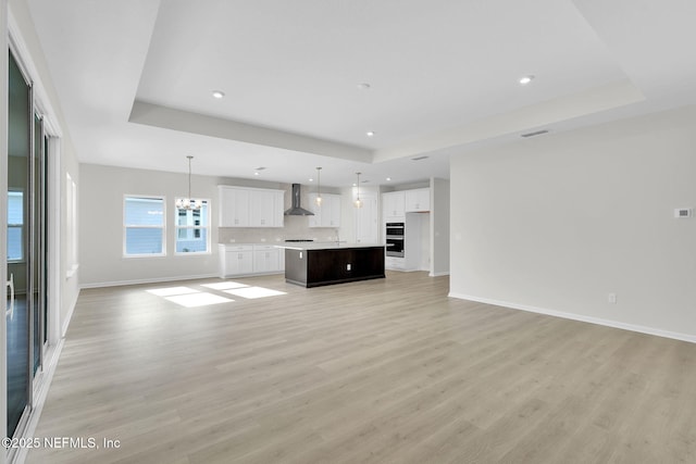 unfurnished living room with a notable chandelier, a tray ceiling, and light hardwood / wood-style flooring