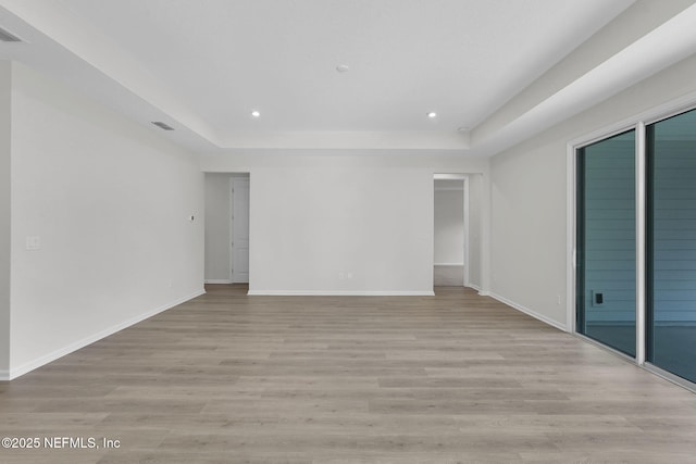 unfurnished room with a tray ceiling and light wood-type flooring