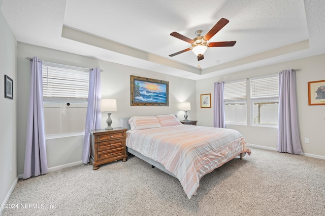 carpeted bedroom featuring a tray ceiling, ceiling fan, and a textured ceiling