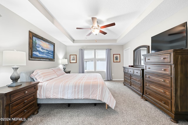 bedroom with ceiling fan, light colored carpet, a textured ceiling, and a raised ceiling