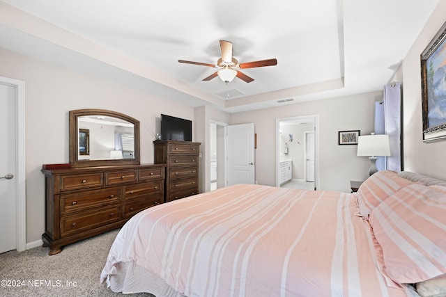 carpeted bedroom featuring a raised ceiling, ceiling fan, and ensuite bathroom