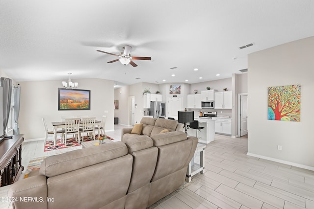 living room featuring ceiling fan with notable chandelier, vaulted ceiling, and light hardwood / wood-style flooring