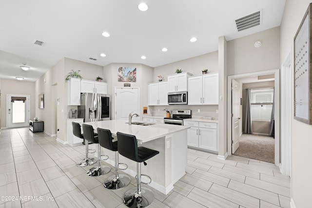 kitchen featuring white cabinets, stainless steel appliances, a kitchen bar, a kitchen island with sink, and sink