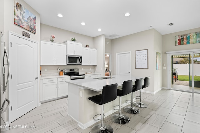 kitchen with a breakfast bar, sink, an island with sink, white cabinetry, and stainless steel appliances