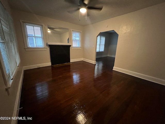 unfurnished living room featuring plenty of natural light, ceiling fan, and dark hardwood / wood-style flooring