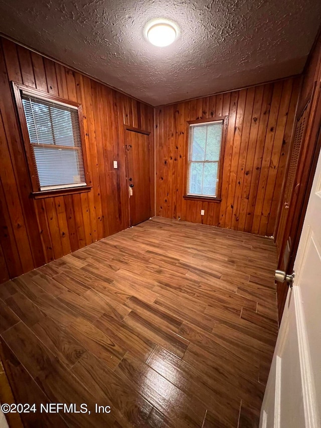 empty room with a textured ceiling, hardwood / wood-style flooring, and wooden walls