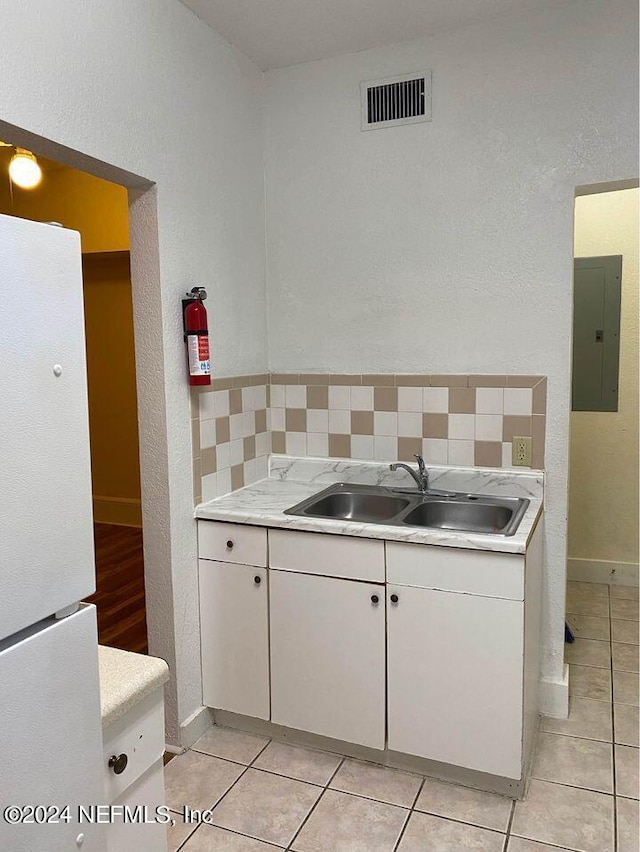 kitchen featuring electric panel, sink, white fridge, light tile patterned flooring, and decorative backsplash