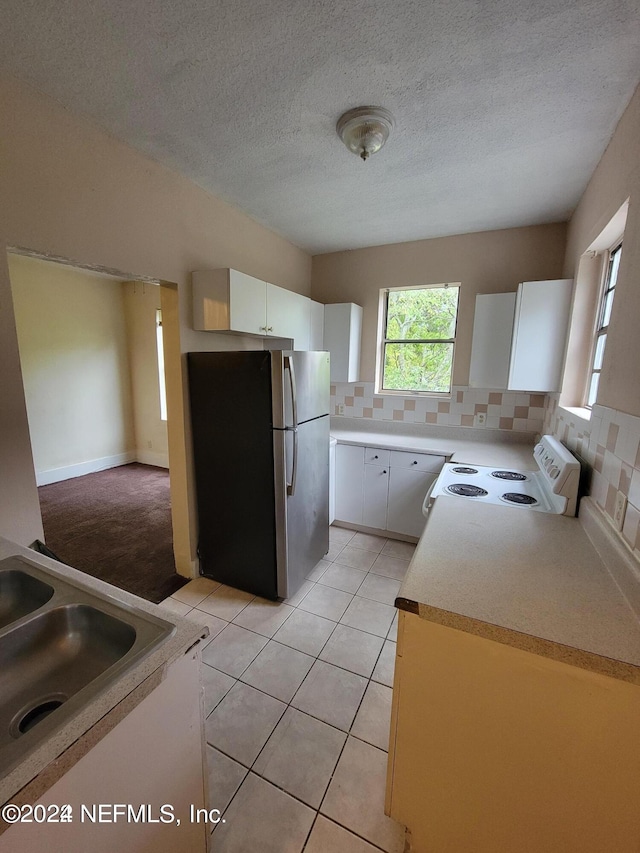 kitchen featuring stainless steel refrigerator, white range, white cabinetry, backsplash, and light colored carpet