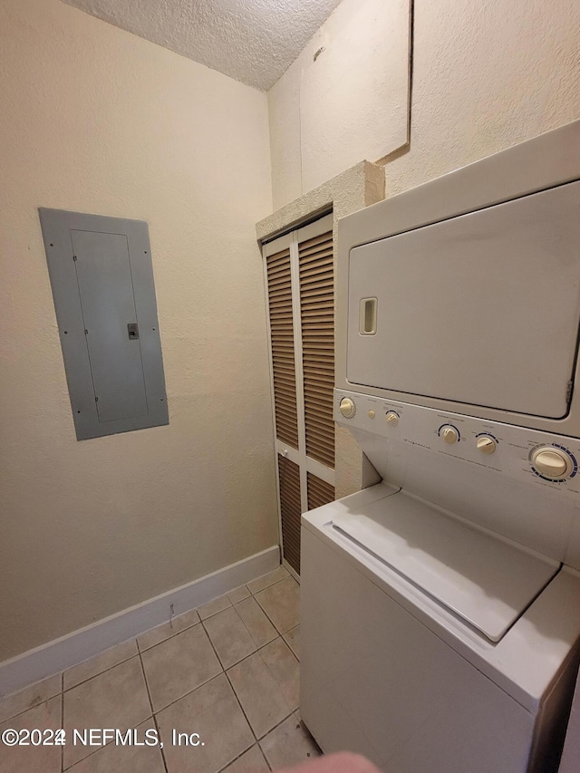 laundry area with light tile patterned flooring, electric panel, a textured ceiling, and stacked washer / drying machine