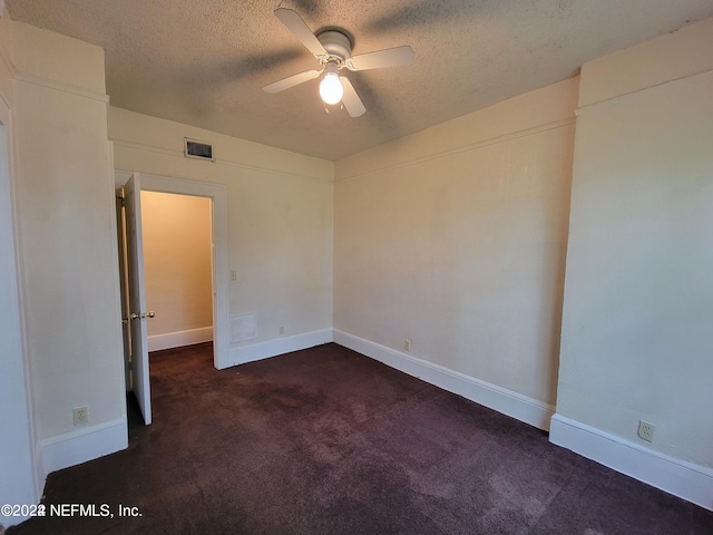 empty room with a textured ceiling, dark colored carpet, and ceiling fan