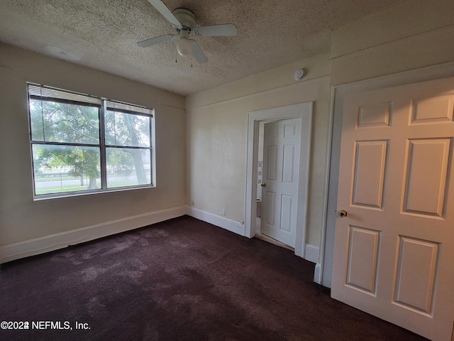 empty room featuring a textured ceiling, dark colored carpet, and ceiling fan