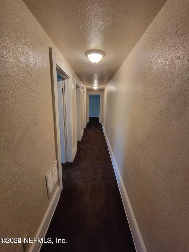 hallway featuring dark colored carpet and a textured ceiling