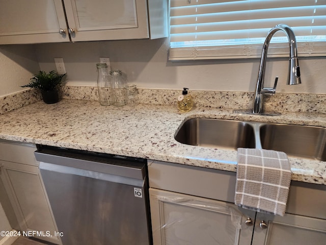 kitchen featuring stainless steel dishwasher, sink, and light stone countertops