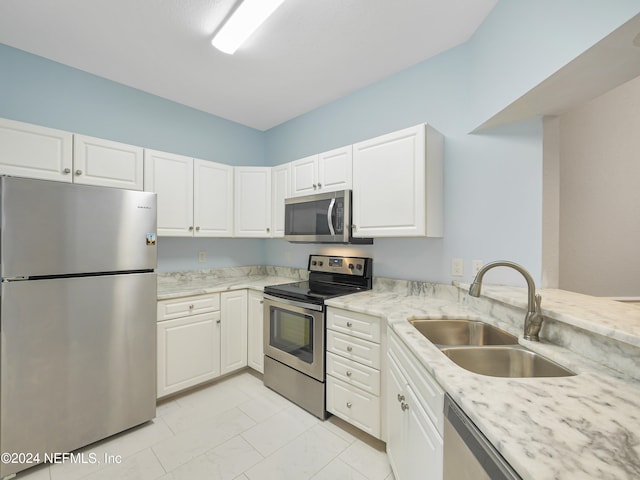 kitchen with light stone countertops, stainless steel appliances, white cabinetry, and sink