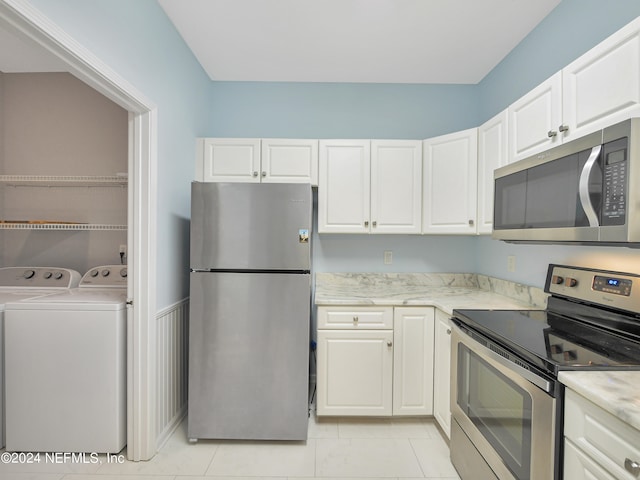 kitchen with appliances with stainless steel finishes, light tile patterned floors, white cabinetry, and washer and clothes dryer