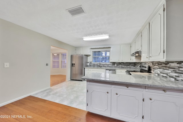 kitchen featuring light wood-type flooring, appliances with stainless steel finishes, white cabinetry, and light stone countertops