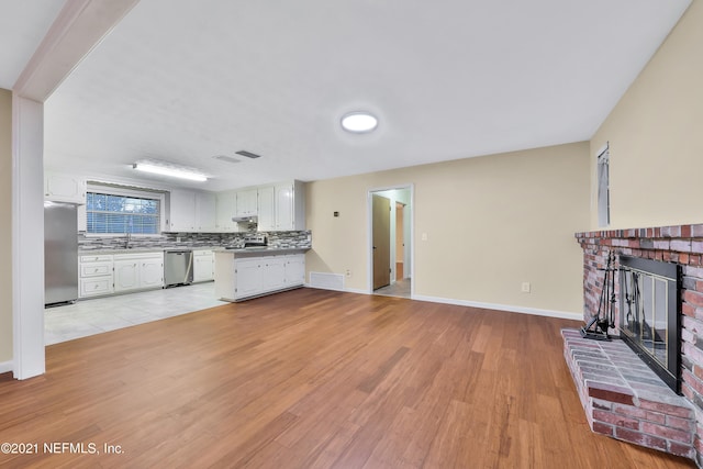 unfurnished living room featuring sink, a brick fireplace, and light hardwood / wood-style flooring