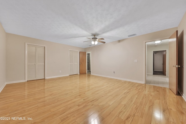 unfurnished bedroom featuring a textured ceiling, ceiling fan, two closets, and light wood-type flooring