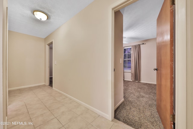 hallway featuring light colored carpet and a textured ceiling