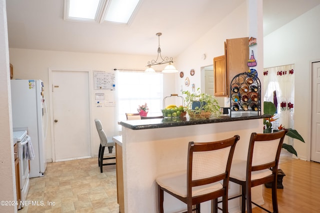 kitchen with a breakfast bar area, lofted ceiling, kitchen peninsula, hanging light fixtures, and white appliances