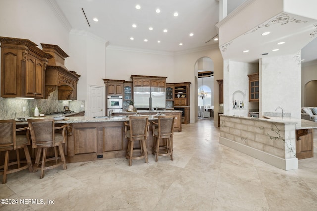 kitchen with a breakfast bar area, ornamental molding, stainless steel appliances, and a towering ceiling