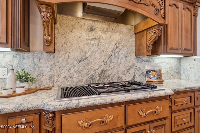 kitchen featuring exhaust hood, light stone counters, stainless steel gas cooktop, and backsplash