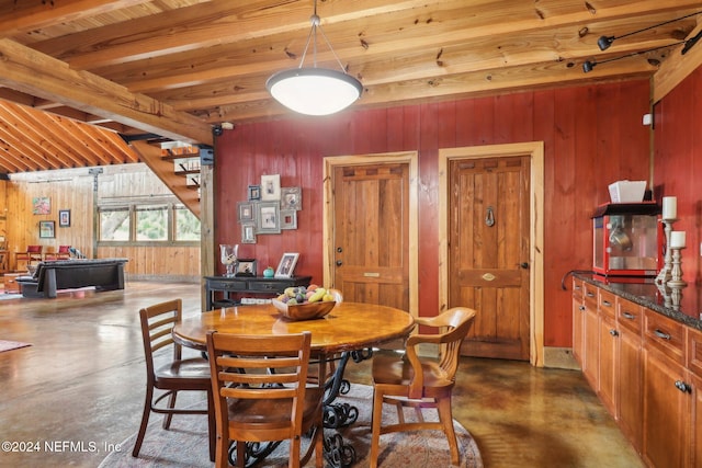 dining area featuring wood walls, finished concrete floors, stairway, and beam ceiling