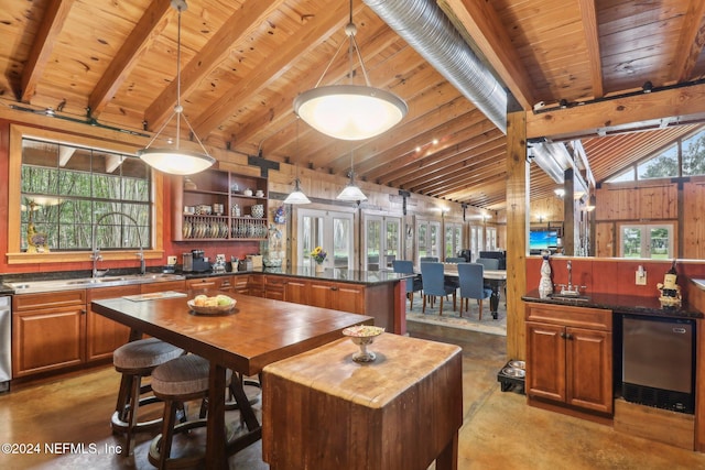 kitchen with brown cabinetry, concrete floors, vaulted ceiling with beams, and a sink