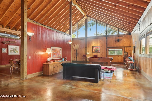 living room with finished concrete flooring, wood walls, baseboards, and high vaulted ceiling