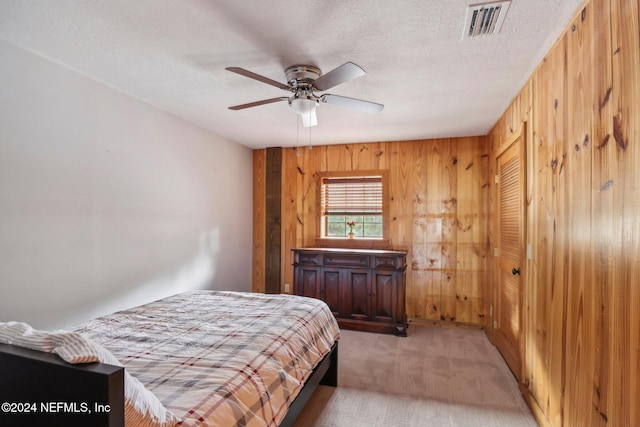 bedroom with a textured ceiling, wood walls, visible vents, and light colored carpet