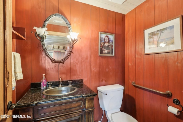 half bath featuring toilet, wooden walls, and vanity