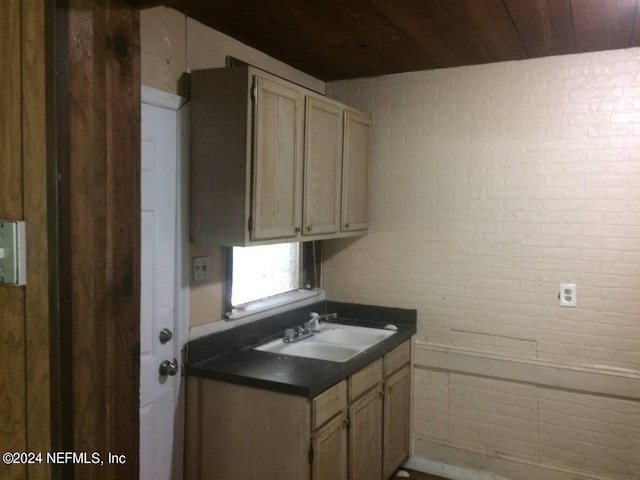 kitchen featuring light brown cabinetry, wood ceiling, brick wall, and sink