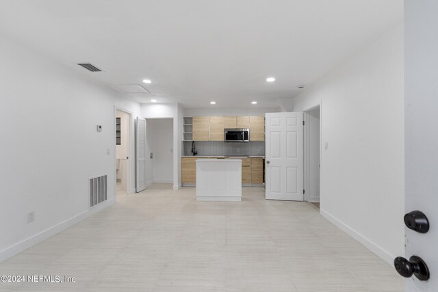 kitchen featuring light brown cabinetry, backsplash, and a center island