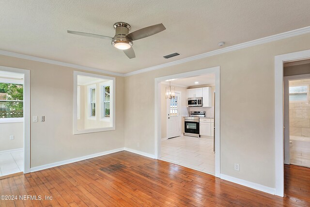 unfurnished room with light wood-type flooring, ceiling fan with notable chandelier, crown molding, and a textured ceiling