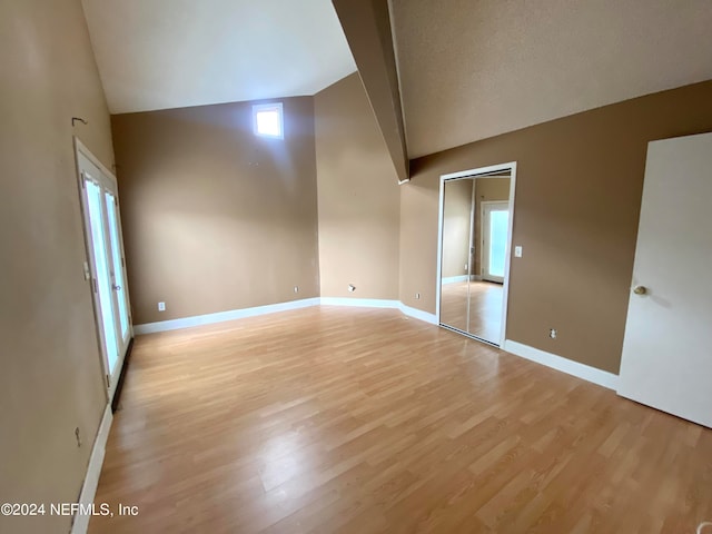 unfurnished room with light hardwood / wood-style floors, vaulted ceiling, and a textured ceiling