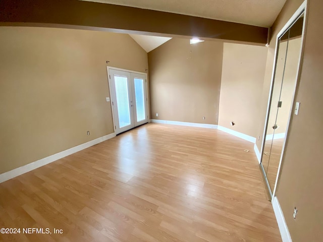 spare room with french doors, vaulted ceiling with beams, and light hardwood / wood-style floors