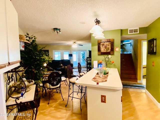 kitchen featuring ceiling fan, hanging light fixtures, a textured ceiling, light hardwood / wood-style flooring, and a breakfast bar area