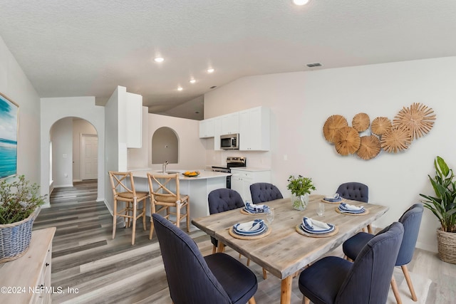 dining space featuring wood-type flooring, a textured ceiling, and vaulted ceiling