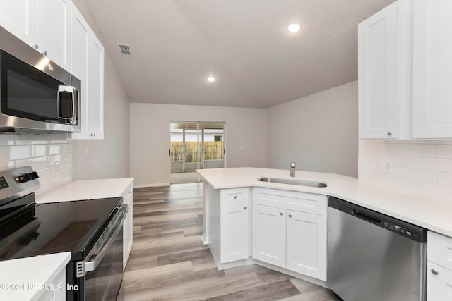 kitchen with light hardwood / wood-style flooring, stainless steel appliances, kitchen peninsula, backsplash, and white cabinetry