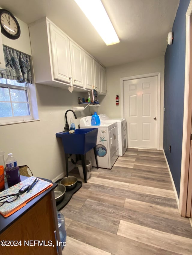 clothes washing area featuring washing machine and dryer, cabinets, and light wood-type flooring