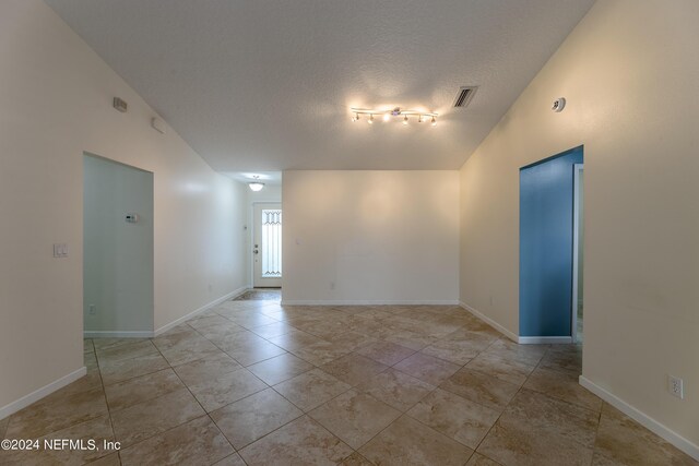 unfurnished room featuring track lighting, a textured ceiling, and vaulted ceiling