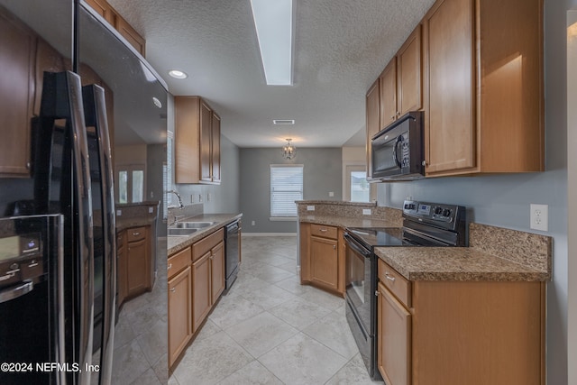 kitchen featuring a textured ceiling, a skylight, light tile patterned floors, black appliances, and sink