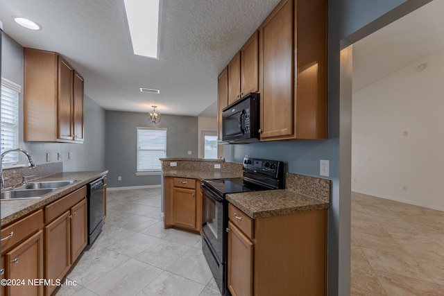 kitchen with a textured ceiling, black appliances, light tile patterned floors, sink, and a skylight