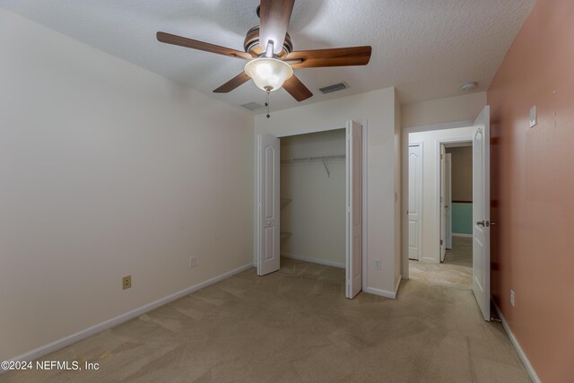 unfurnished bedroom featuring a closet, ceiling fan, light carpet, and a textured ceiling