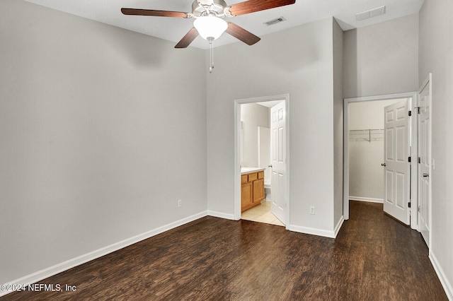 unfurnished bedroom featuring connected bathroom, ceiling fan, a closet, dark wood-type flooring, and a walk in closet