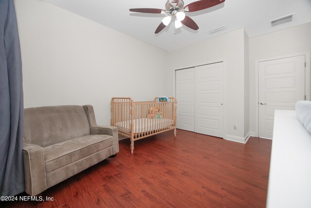 bedroom with ceiling fan, dark wood-type flooring, a nursery area, and a closet