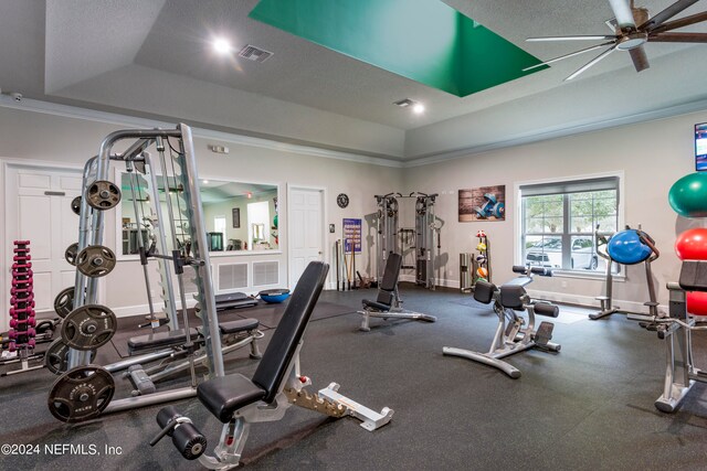 workout area with ceiling fan, a textured ceiling, and a tray ceiling