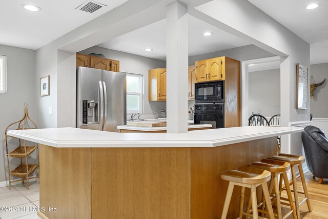 kitchen featuring light hardwood / wood-style flooring, a kitchen bar, and black appliances