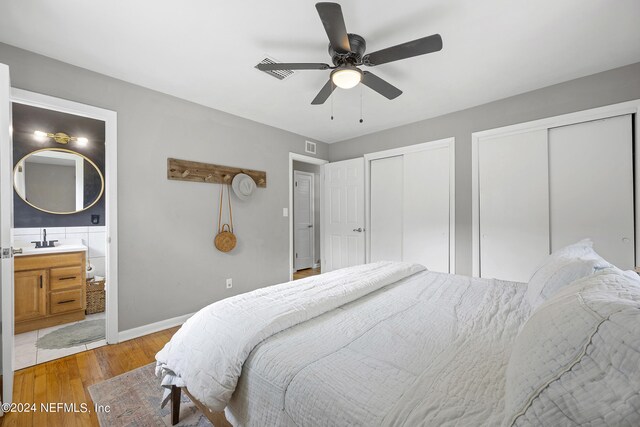 bedroom with ceiling fan, sink, multiple closets, light wood-type flooring, and ensuite bath