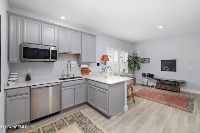 kitchen featuring light hardwood / wood-style flooring, kitchen peninsula, stainless steel appliances, and sink